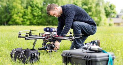 Young Engineer Setting SLR Camera On UAV Helicopter At Park